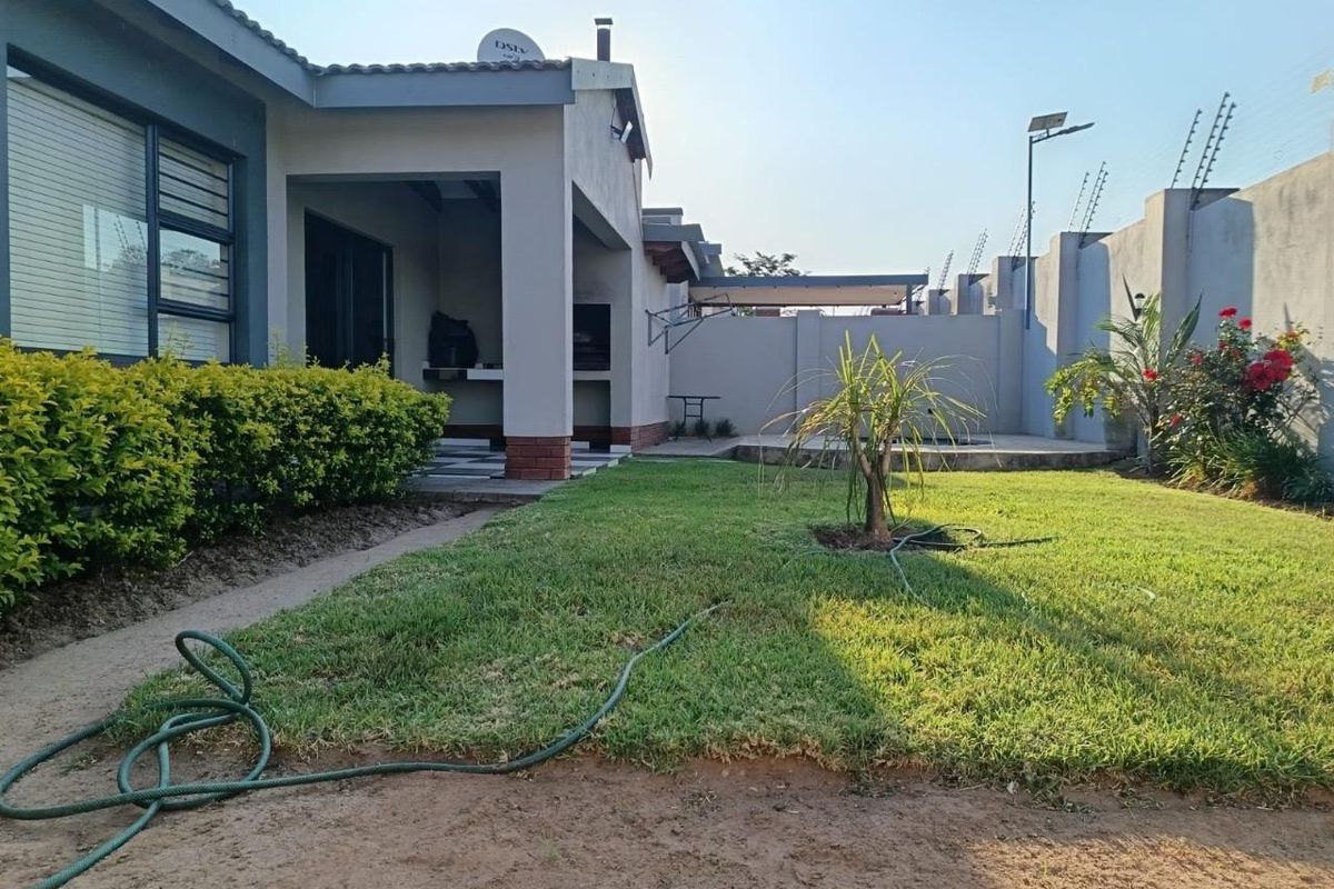 Rear view of the townhouse featuring a covered patio with a built-in braai, a private garden, and secure perimeter walling with electric fencing.