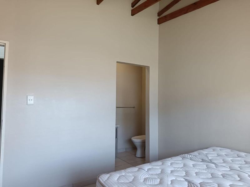 A bedroom featuring exposed timber rafters and an en-suite bathroom, offering a neutral canvas for personalization.