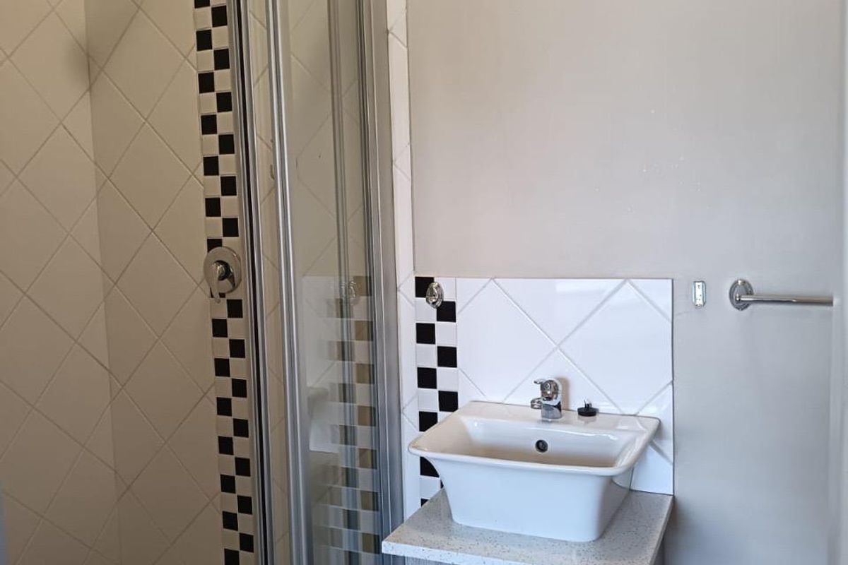 A compact bathroom featuring a shower enclosure with decorative tile accents and a modern vessel sink set on a wood-look vanity cabinet.