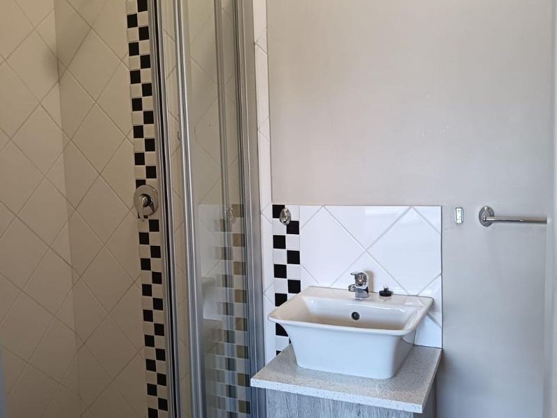 A compact bathroom featuring a shower enclosure with decorative tile accents and a modern vessel sink set on a wood-look vanity cabinet.
