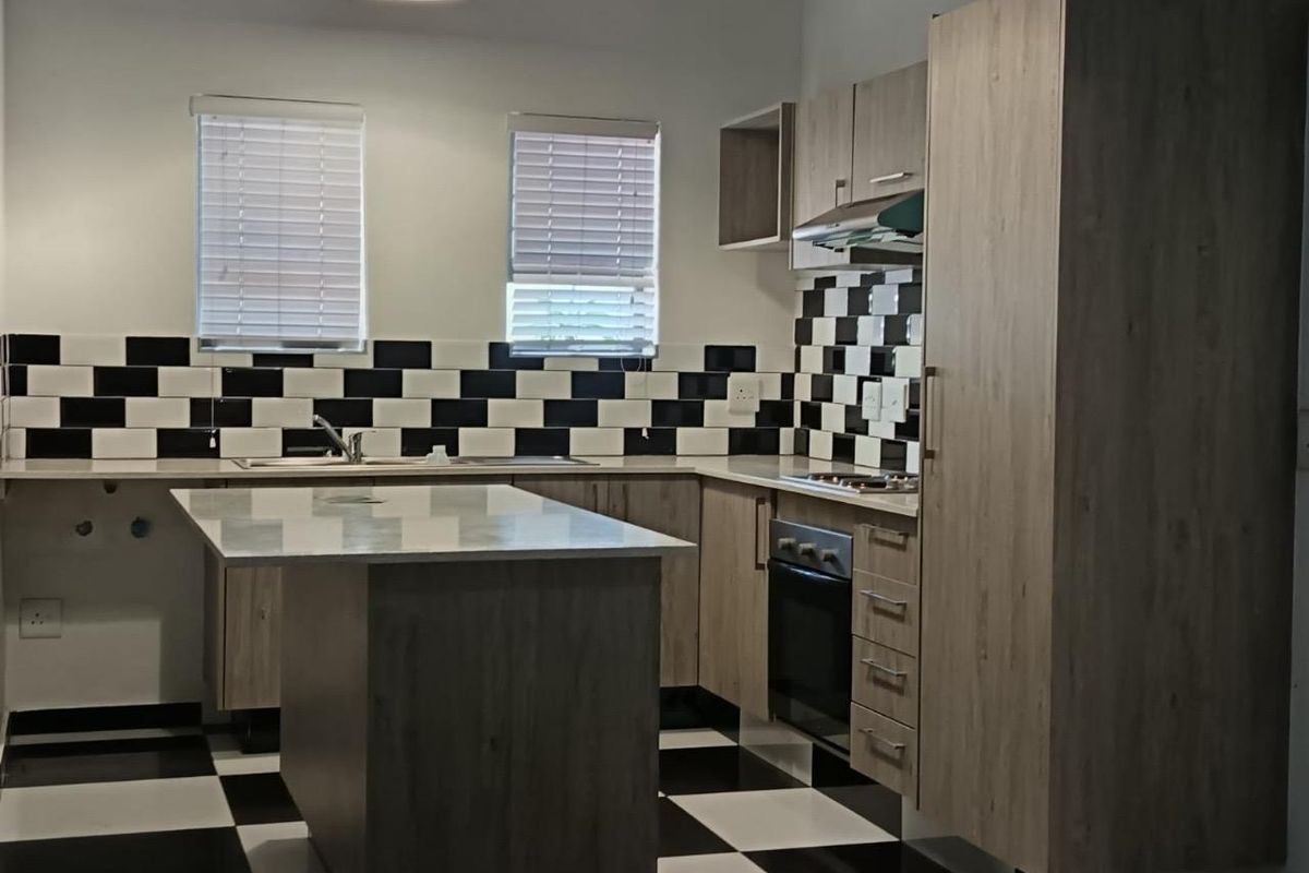 Modern kitchen featuring light wood-grain cabinetry, a central island, built-in oven and hob, and a distinctive black and white checkered tile backsplash and flooring.