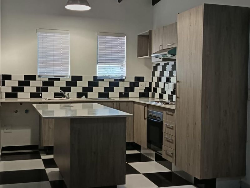 Modern kitchen featuring light wood-grain cabinetry, a central island, built-in oven and hob, and a distinctive black and white checkered tile backsplash and flooring.