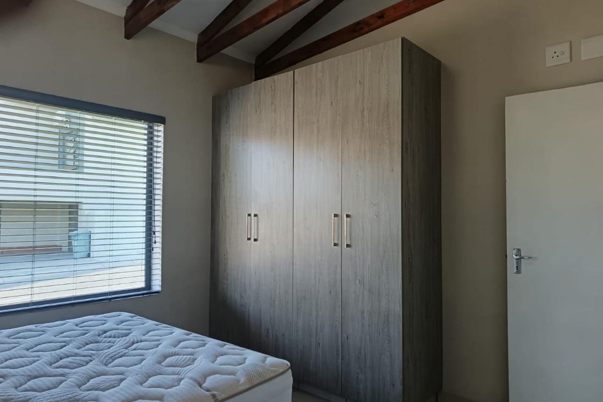 A well-maintained bedroom featuring exposed timber rafters, built-in cupboards with a wood-grain finish, and venetian blinds for privacy.
