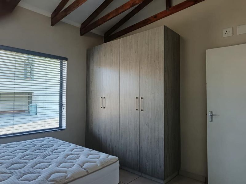 A well-maintained bedroom featuring exposed timber rafters, built-in cupboards with a wood-grain finish, and venetian blinds for privacy.