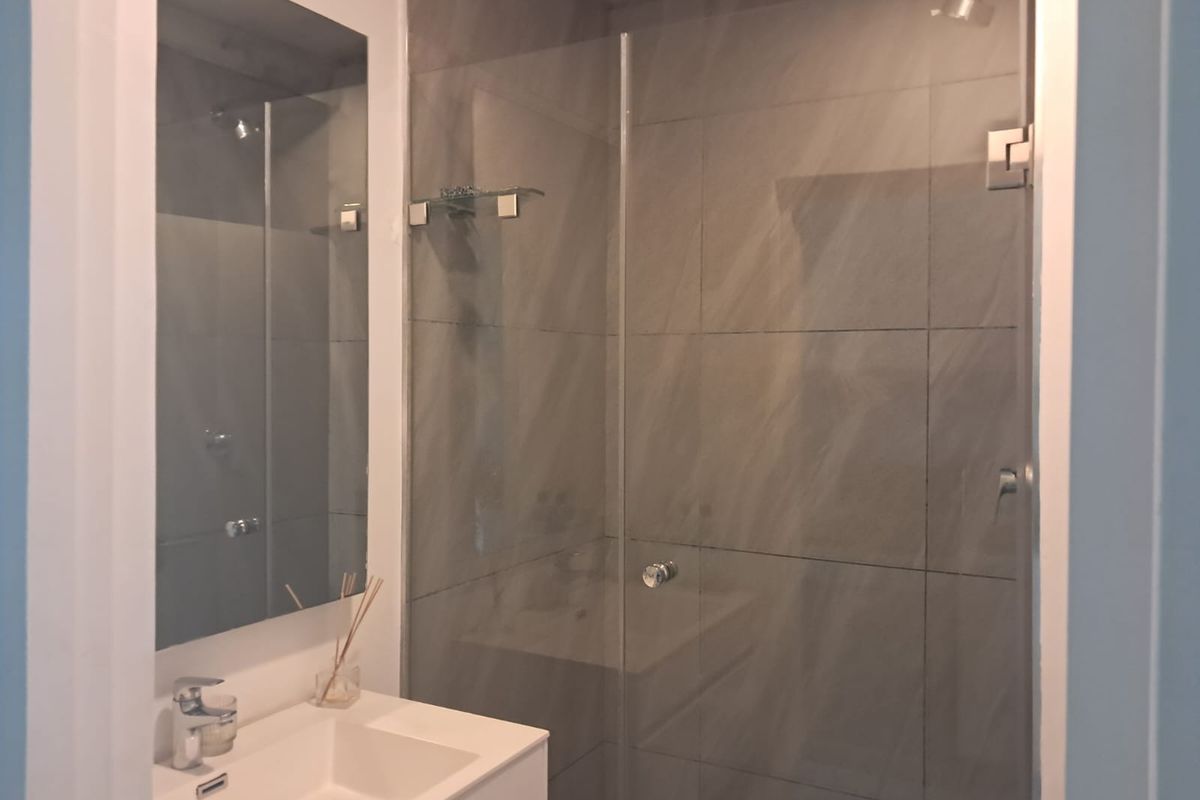 A modern bathroom featuring a sleek vanity with integrated sink, wall-mounted mirror, and a spacious walk-in shower with glass screen and tiled walls.