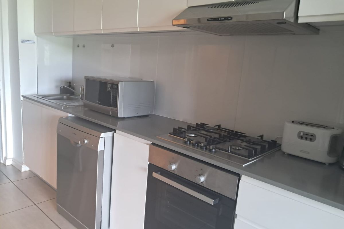 Modern kitchen featuring white cabinetry, stone countertops, stainless steel gas hob, built-in oven, extractor fan, and tiled flooring.