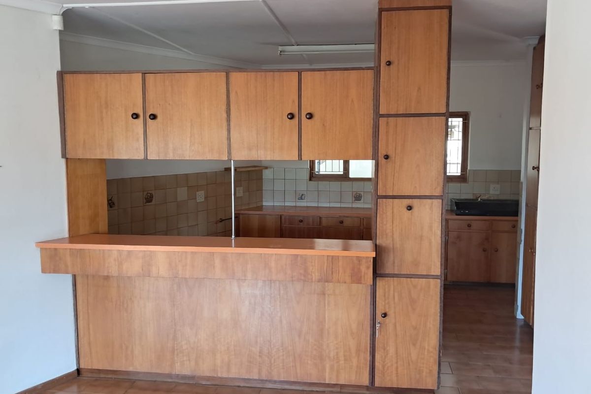 A dated kitchen featuring wood-look cabinetry, a breakfast bar, and tiled splashbacks, offering a functional layout ready for modernization.
