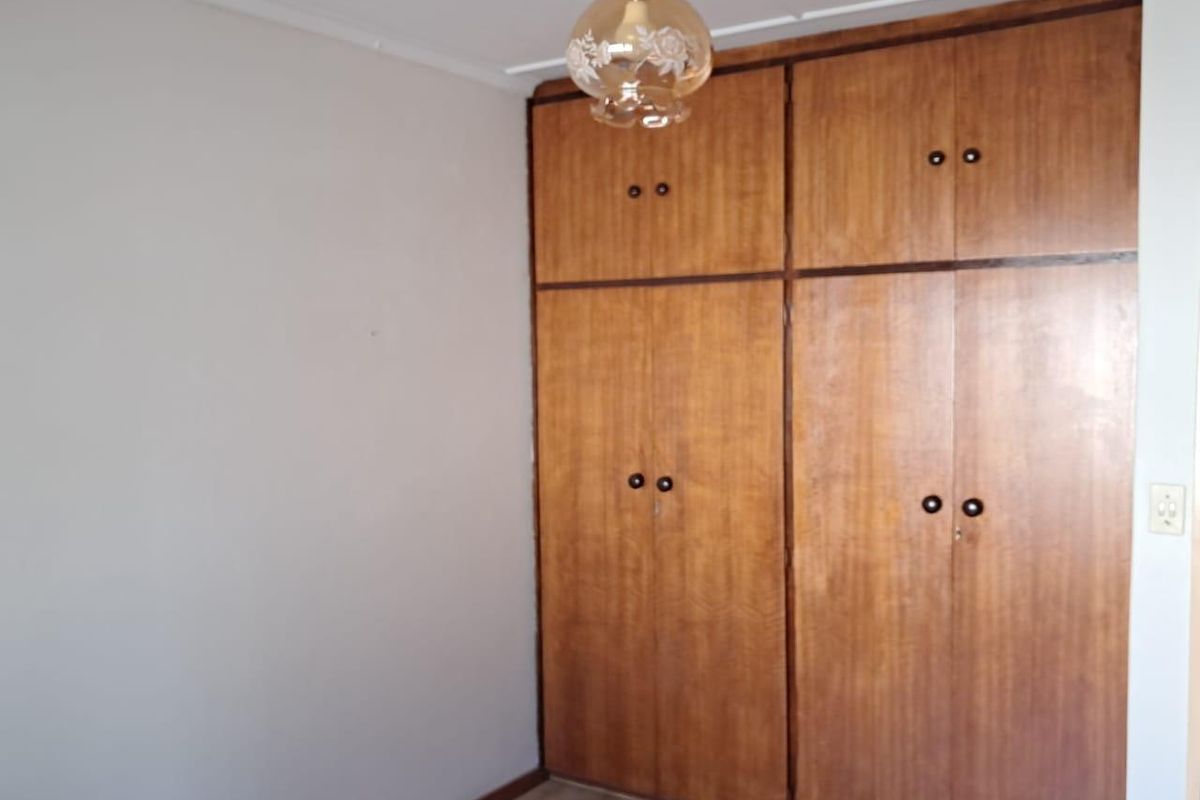 A bedroom featuring built-in wooden cupboards with classic hardware and a neutral wall finish.