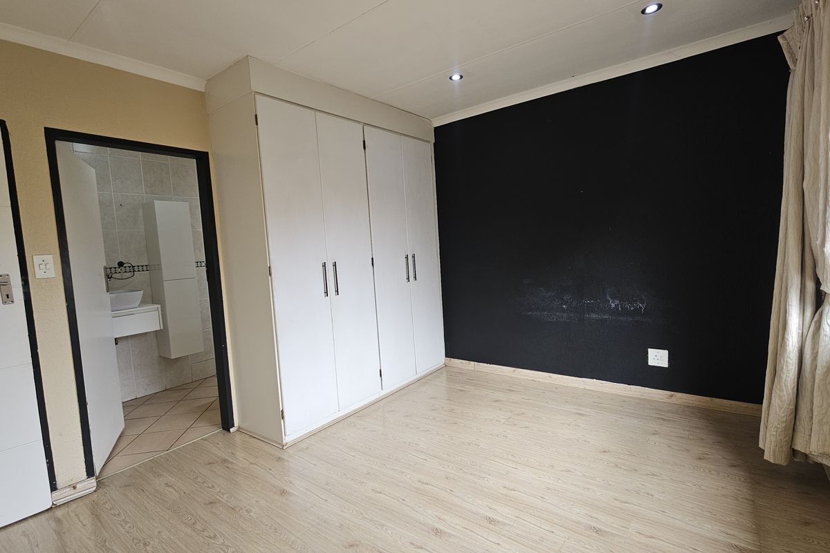 A bedroom featuring laminate flooring, built-in cupboards, and an en-suite bathroom. The room is vacant and ready for personalization.