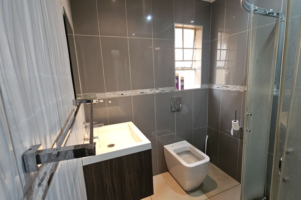 Modern bathroom featuring a wall-mounted vanity, wall-hung toilet, and a glass-enclosed shower with contemporary grey wall tiling.