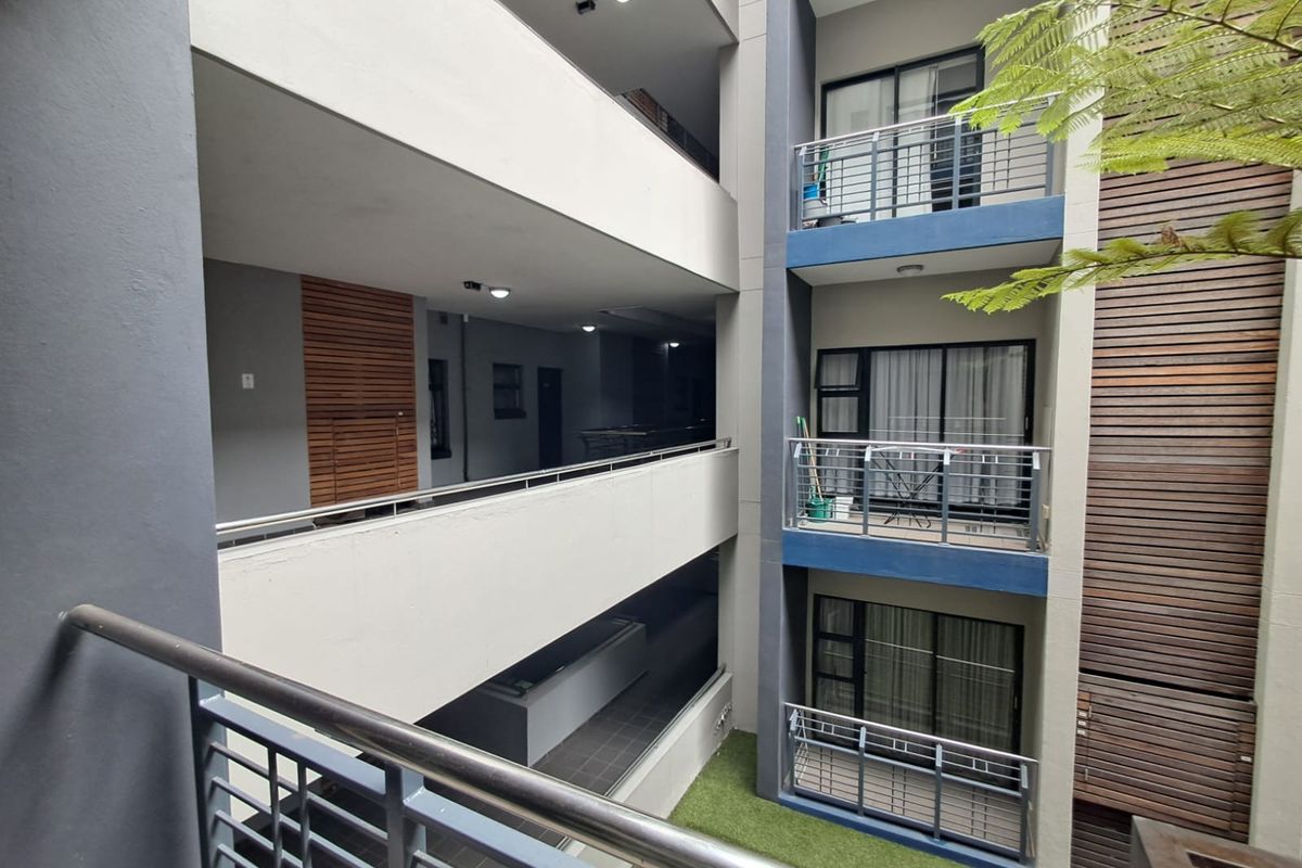 View of the apartment complex exterior featuring stacked balconies with metal railings, sliding glass doors, and modern timber cladding accents.
