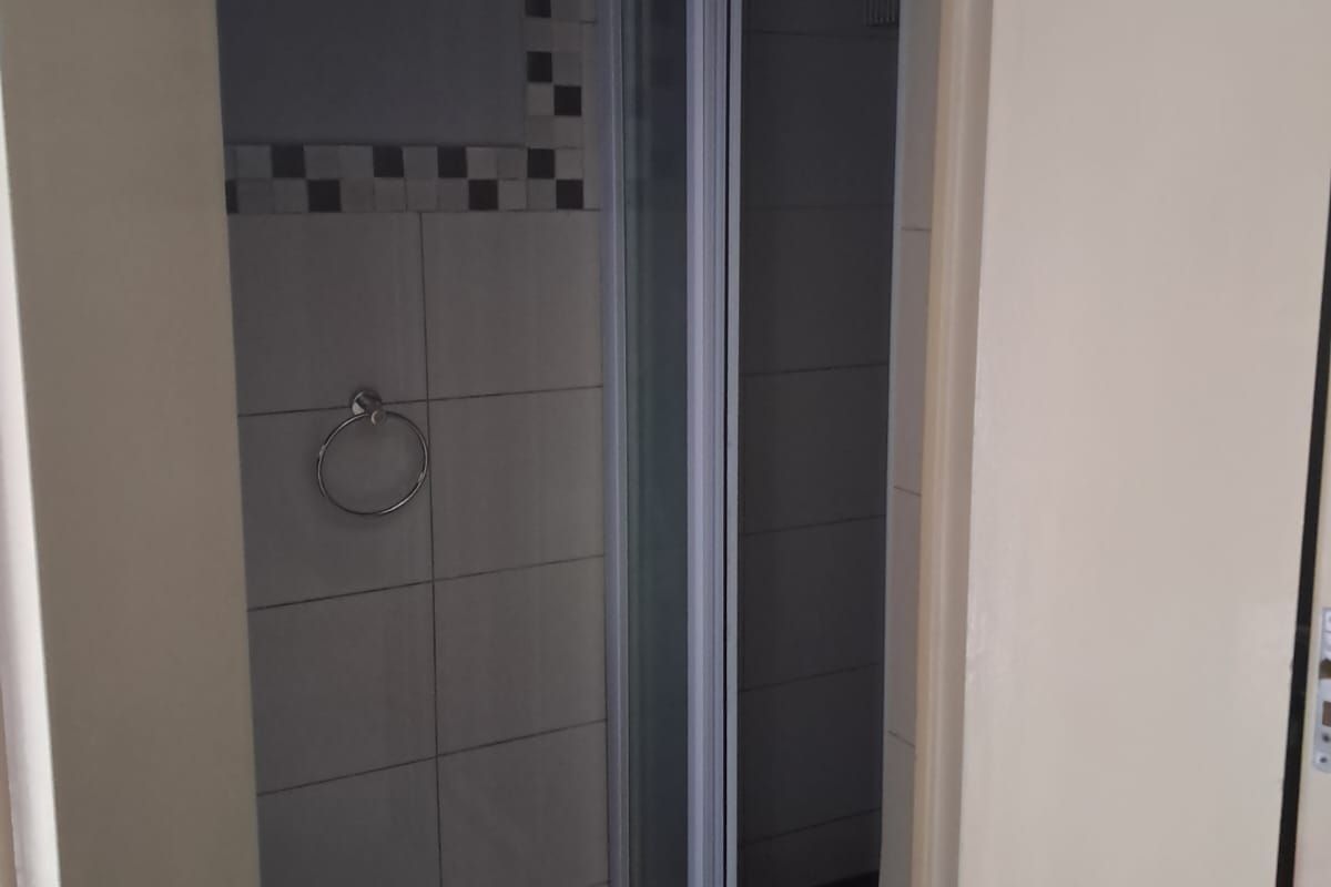 A compact bathroom featuring a shower enclosure with tiled walls and flooring, including a wall-mounted towel ring.