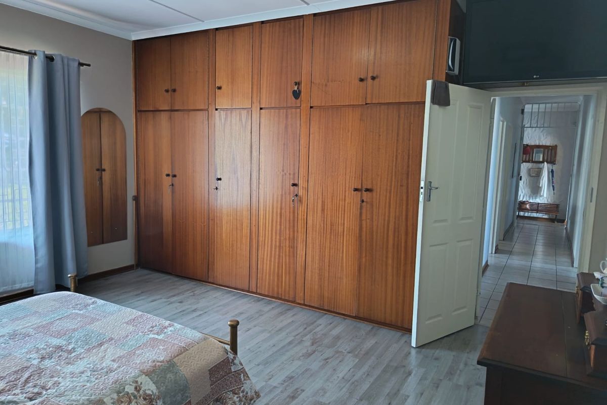 A bedroom featuring extensive floor-to-ceiling built-in wooden cabinetry and modern laminate flooring, offering ample storage space.