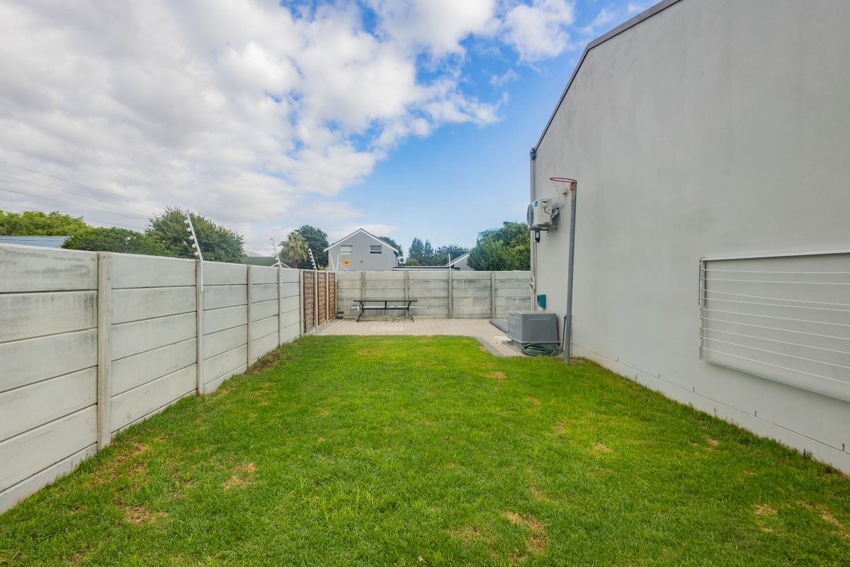 A private rear garden featuring a lawn, paved patio area, and secure boundary walling with electric fencing.