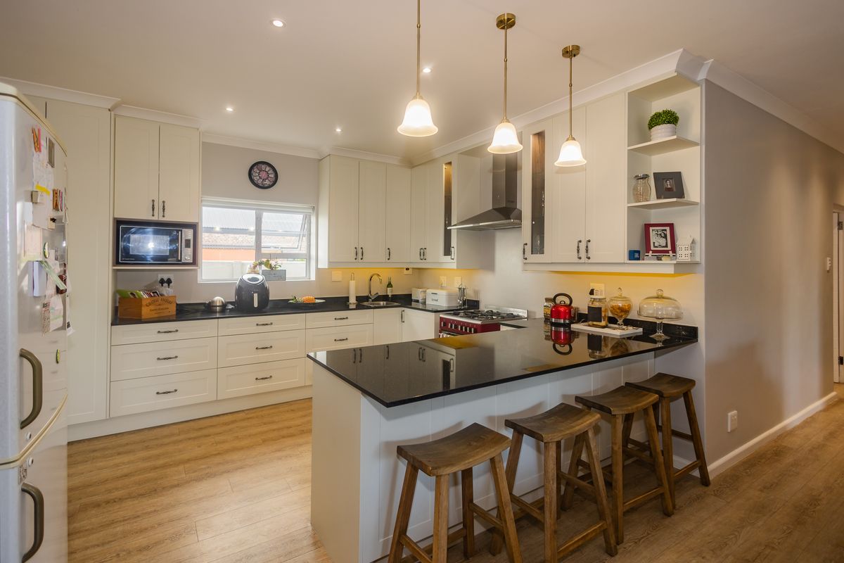 Modern kitchen featuring white cabinetry, black granite countertops, a breakfast bar, integrated appliances, and warm pendant lighting.