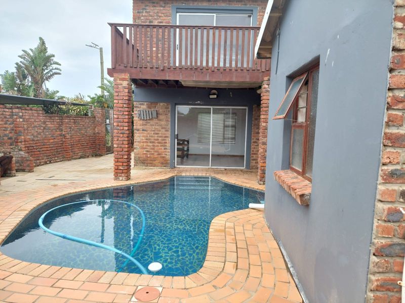 Rear exterior view featuring a swimming pool with brick surround, a raised timber balcony, and brick wall finishes.