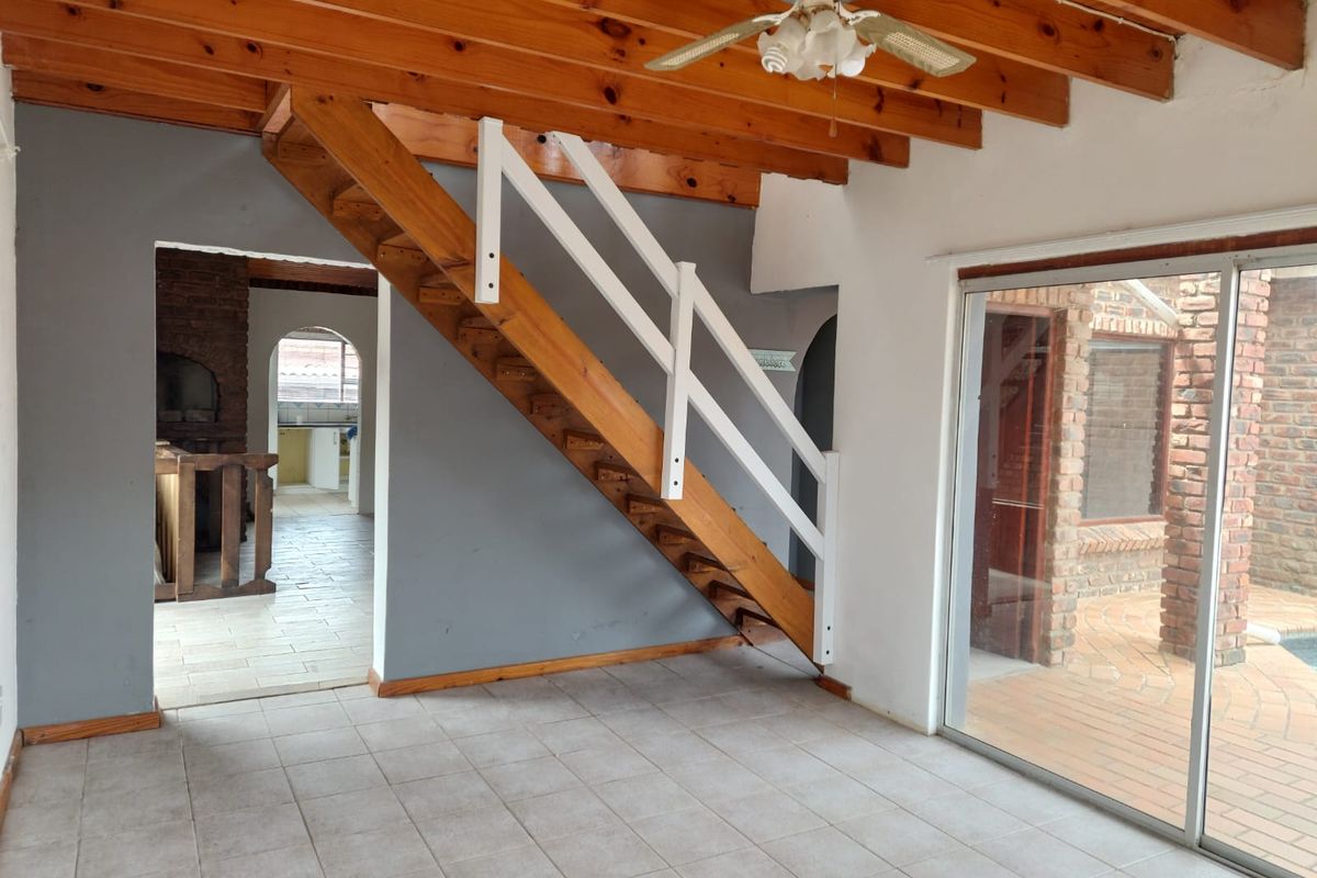 Spacious living area featuring exposed timber ceiling beams, a central staircase, and large sliding glass doors leading to an outdoor patio area.