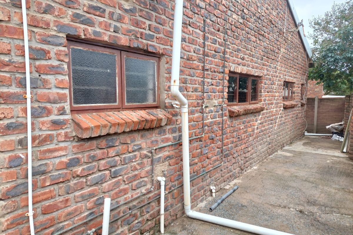 Rear exterior view of the property featuring exposed brick walls, steel-framed windows, and external plumbing infrastructure along a concrete walkway.