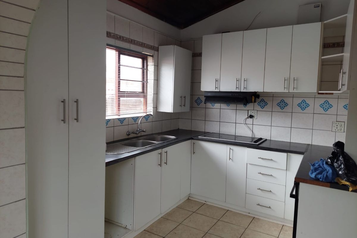 A functional kitchen featuring white built-in cabinetry, a double bowl sink, electric hob, extractor fan, and tiled finishes throughout.
