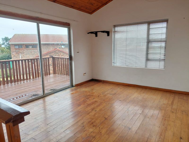 An empty living room featuring timber flooring, a vaulted timber ceiling, and a sliding glass door providing access to an outdoor deck.