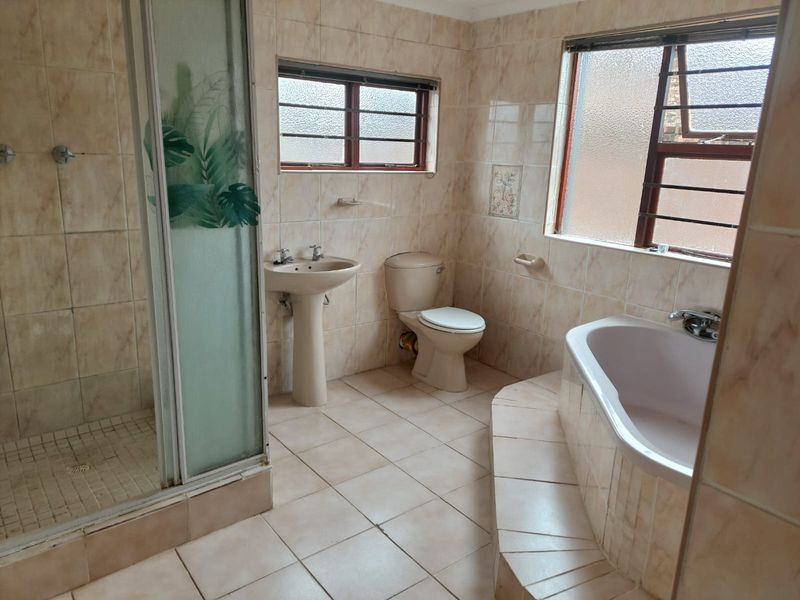 A spacious bathroom featuring a built-in bathtub, separate shower enclosure, pedestal basin, and toilet, finished with neutral wall and floor tiling.