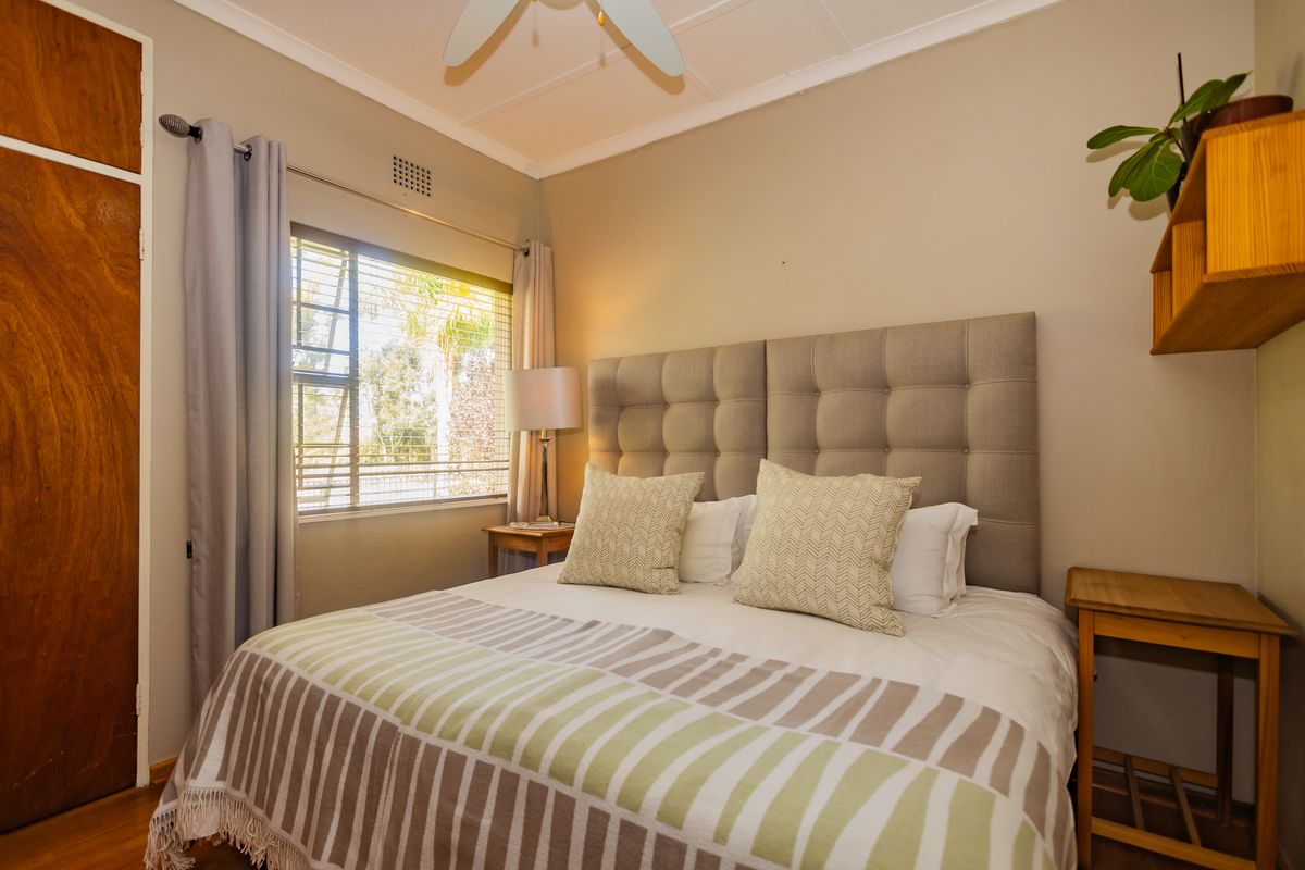 A well-maintained bedroom featuring timber flooring, a ceiling fan, and a built-in cupboard, offering a comfortable and functional living space.