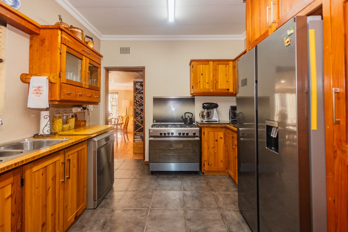 A functional kitchen featuring warm wooden cabinetry, tiled flooring, a gas stove with extractor, and a convenient built-in wine rack in the adjacent area.