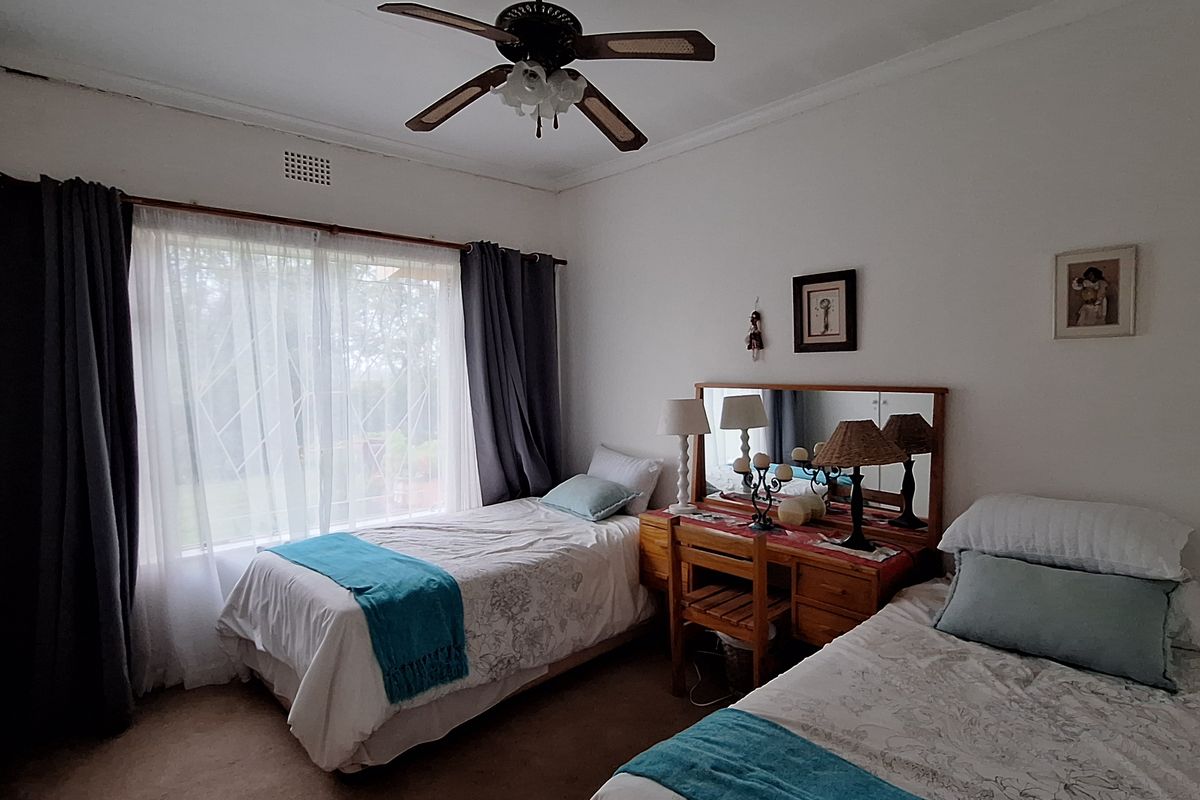 A bedroom featuring a ceiling fan, large window with curtains, and carpeted flooring.