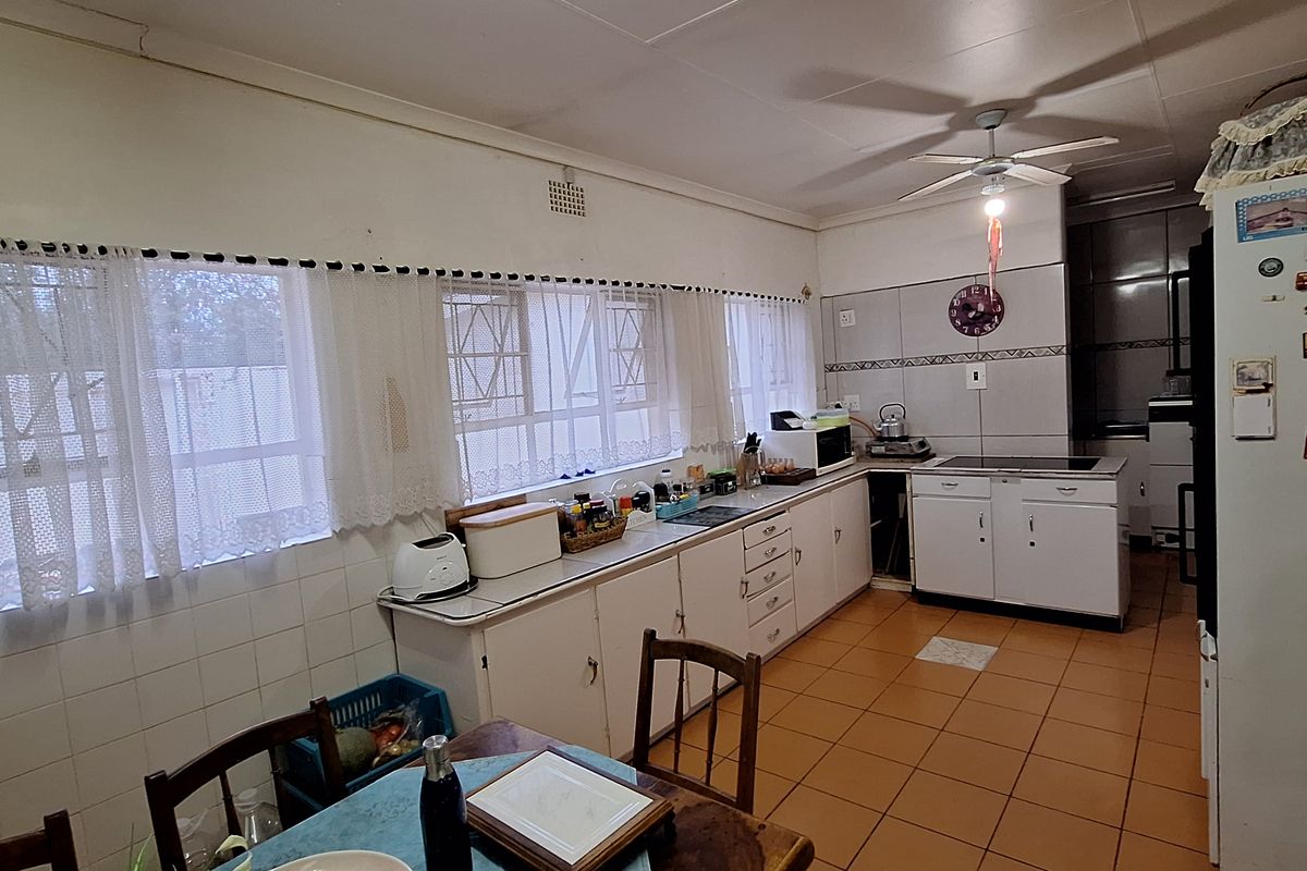 A dated kitchen featuring original cabinetry, tiled flooring, and a functional layout with ample counter space and natural light from multiple windows.