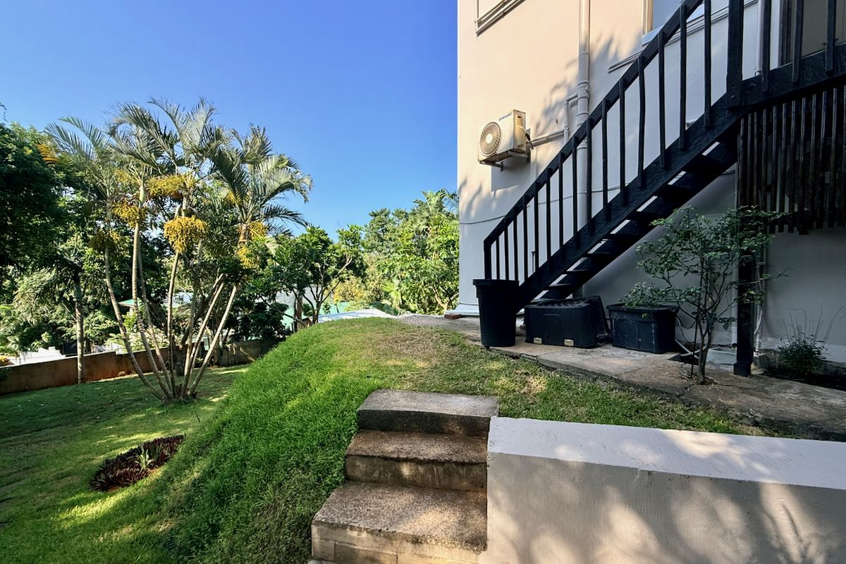 Rear exterior view featuring a landscaped garden, concrete steps, and an external staircase leading to the upper level of the property.