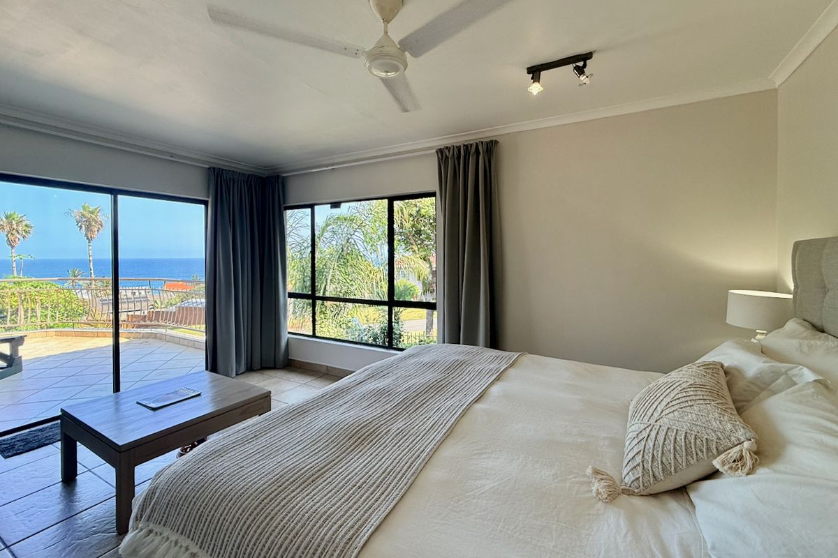 Spacious bedroom featuring tiled flooring, ceiling fan, and large sliding glass doors opening onto a patio with scenic ocean views.