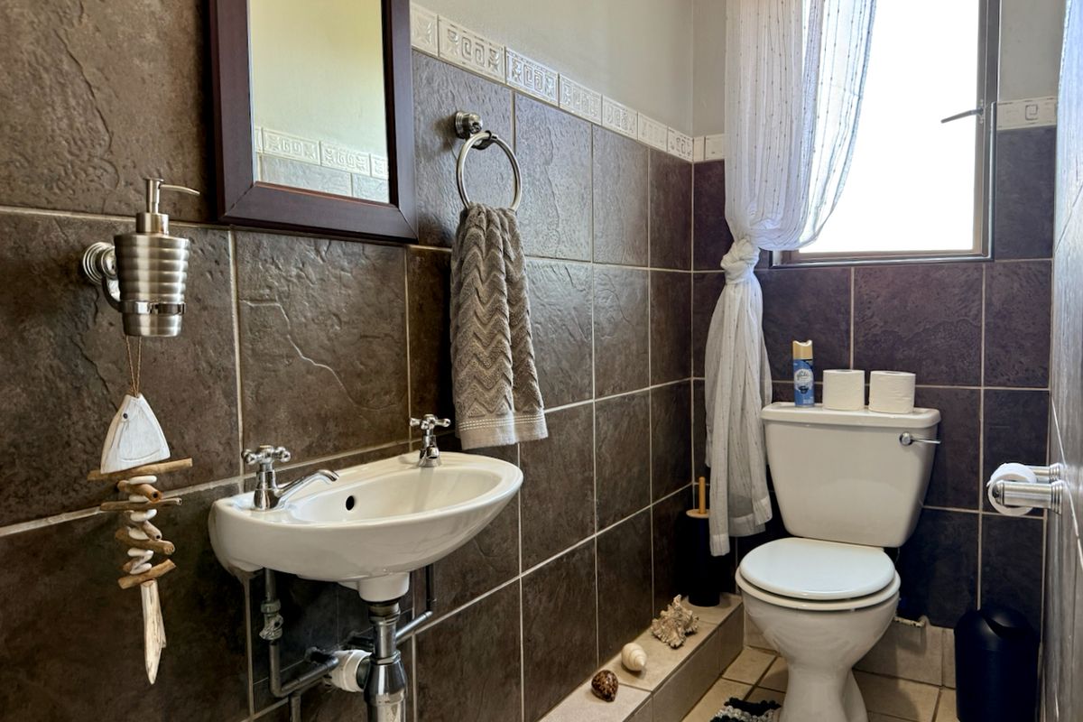 A functional bathroom featuring dark brown wall tiles, a wall-mounted basin, and a standard toilet with a window for natural light.