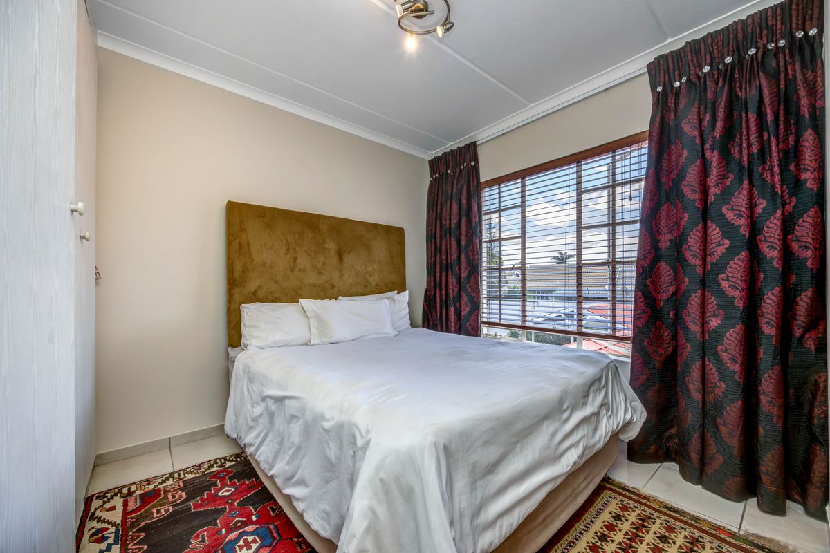 A functional bedroom featuring tiled flooring, a built-in cupboard, and large windows with venetian blinds, offering a comfortable and practical living space.