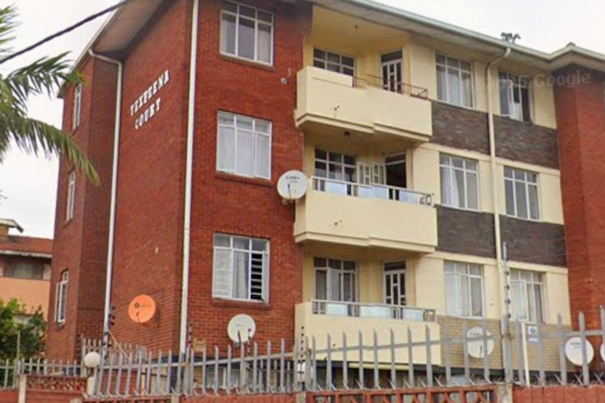 Exterior view of a multi-story brick apartment building featuring private balconies, secure perimeter walling, and electric fencing.