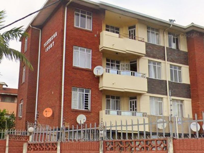 Exterior view of a multi-story brick apartment building featuring private balconies, secure perimeter walling, and electric fencing.