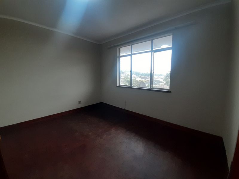 An empty bedroom featuring dark wooden flooring, neutral walls, and a large window providing natural light and an exterior view.