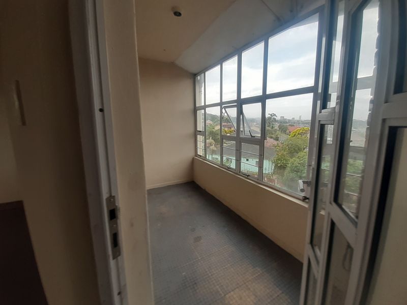 An enclosed balcony or sunroom featuring large aluminium-framed windows, tiled flooring, and elevated views of the surrounding neighbourhood.