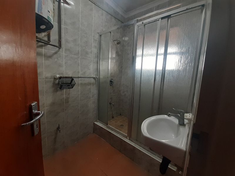 A functional bathroom featuring a shower enclosure, wall-mounted basin, and tiled finishes, offering potential for modernization and aesthetic improvement.