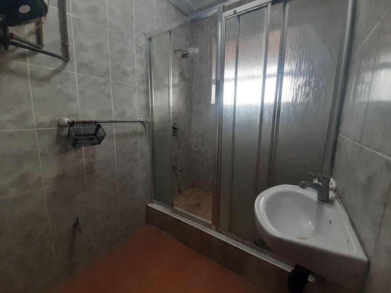 A functional bathroom featuring a shower enclosure, pedestal basin, and tiled finishes, currently in need of cosmetic updates and modernization.
