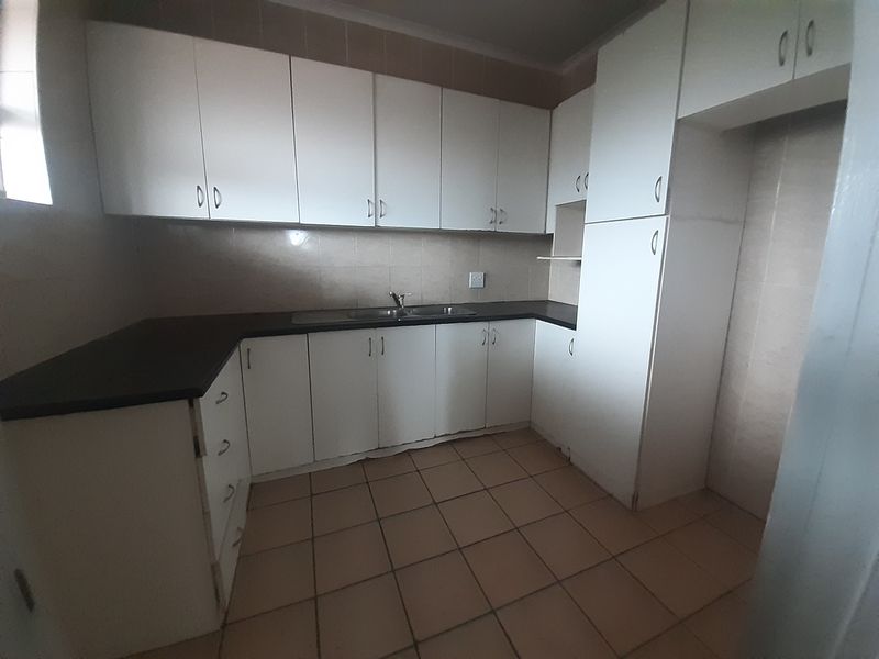A functional, empty kitchen featuring white built-in cabinetry, dark laminate countertops, a double sink, and tiled flooring, offering a blank canvas for renovation.