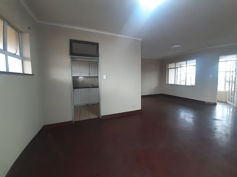 Spacious open-plan living area featuring tiled floors and large windows, with an adjacent separate kitchen area.