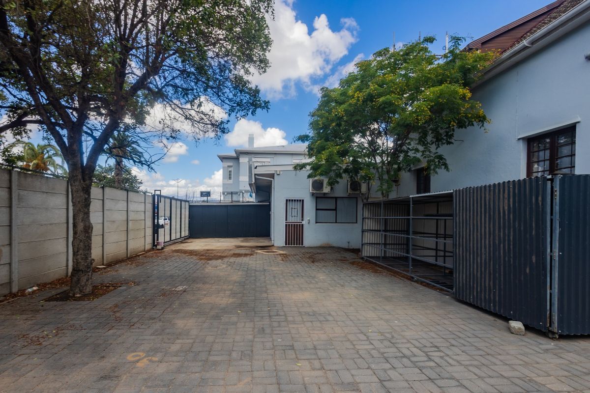 A paved rear exterior area featuring a boundary wall, metal storage structure, and wall-mounted air conditioning units.