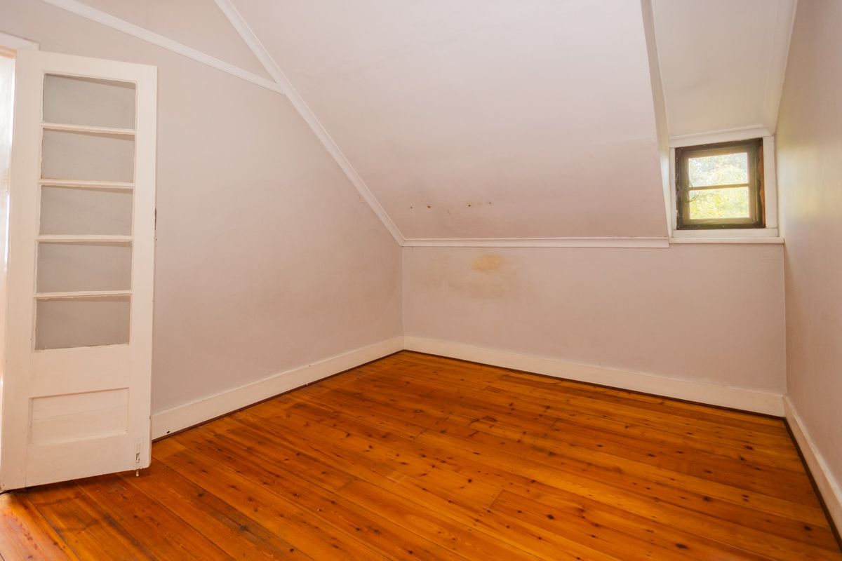 An empty bedroom featuring sloped ceilings, polished timber flooring, and a classic multi-pane window, offering a blank canvas for renovation.