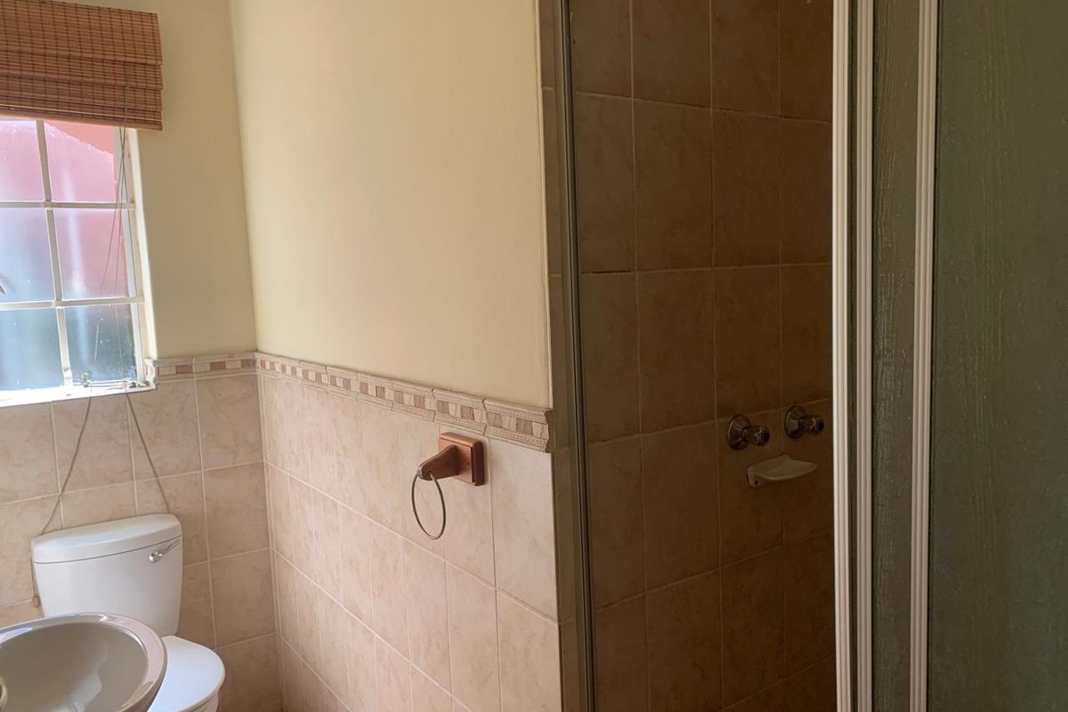A functional bathroom featuring a shower enclosure, pedestal basin, and toilet with neutral ceramic wall tiling.