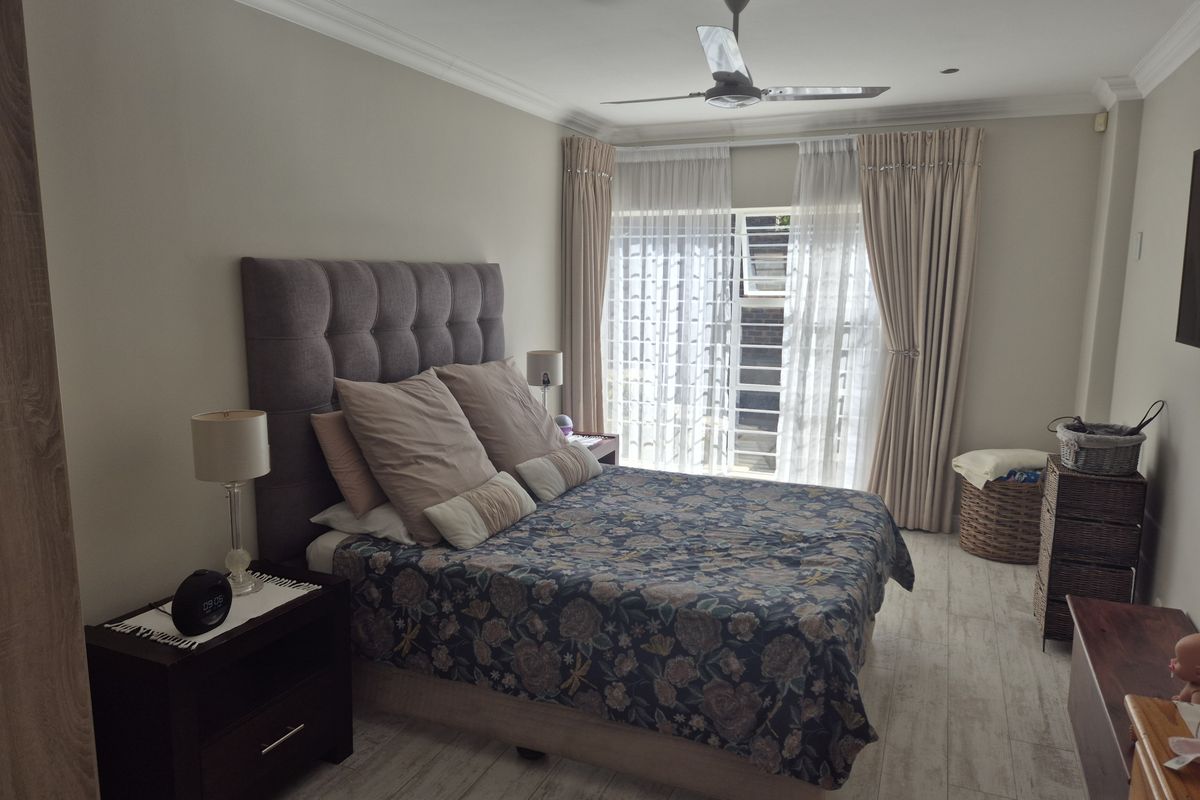 A well-maintained bedroom featuring wood-look tile flooring, a ceiling fan, and large windows with curtains allowing for natural light.