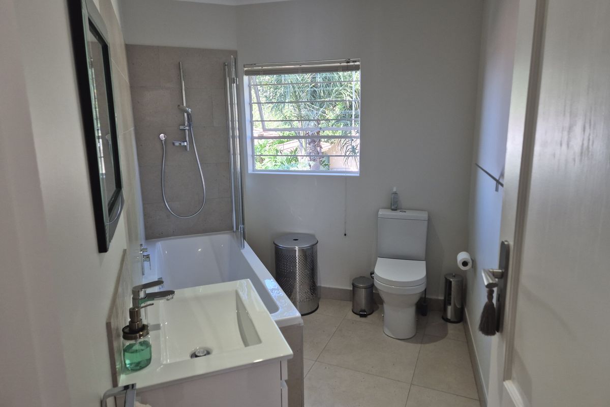 A functional bathroom featuring a built-in bathtub with shower mixer, a modern vanity basin, and a standard toilet with tiled flooring.