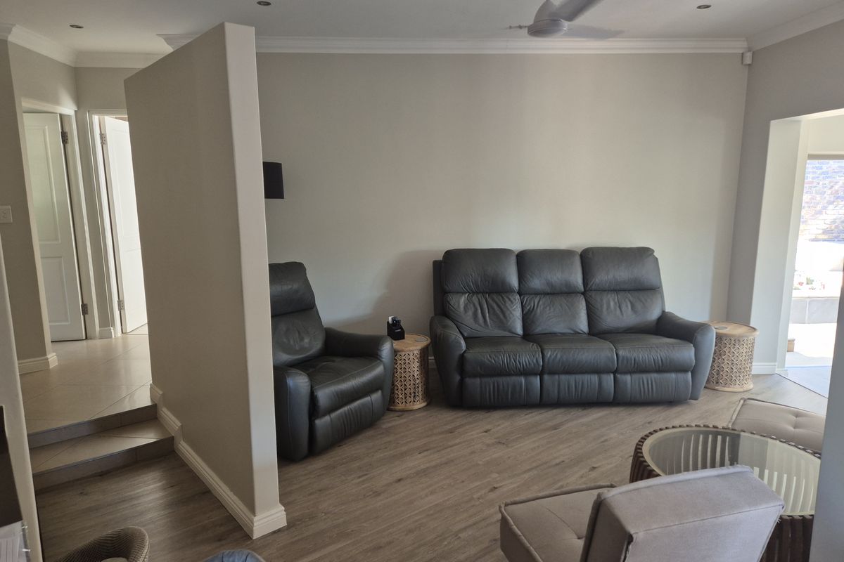 A spacious living room featuring wood-look flooring, a ceiling fan, and a partial partition wall creating a distinct seating area.