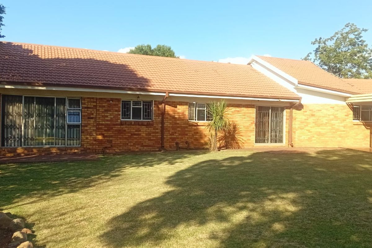 Rear view of a single-story brick house featuring a tiled roof, sliding glass doors with security gates, and a spacious lawn area.