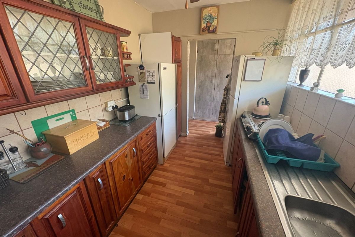 A functional kitchen featuring wooden cabinetry, laminate countertops, a stainless steel sink, and tiled backsplash, offering potential for a modern renovation.
