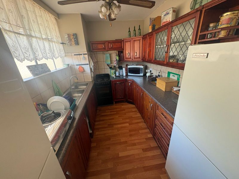 A dated kitchen featuring wooden cabinetry, laminate countertops, a double basin sink, and tiled backsplash, offering potential for a modern renovation.